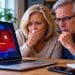 Concerned older couple looking at a laptop displaying a suspicious red malware warning at home